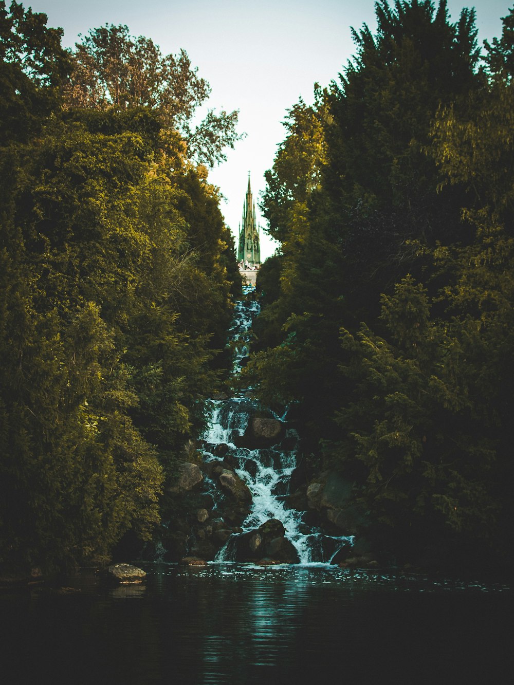 a waterfall in the middle of a forest with a church in the background