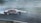 A vintage car with 'NANOPROTEC' branding is drifting on a race track, creating a plume of white smoke. The track has visible tire marks and is surrounded by blue and white barriers. The scene captures the dynamic motion and excitement of motorsport.