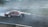 A vintage car with 'NANOPROTEC' branding is drifting on a race track, creating a plume of white smoke. The track has visible tire marks and is surrounded by blue and white barriers. The scene captures the dynamic motion and excitement of motorsport.