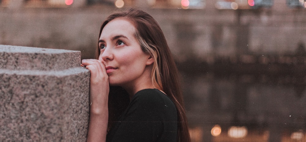 a woman leaning against a stone wall with her hand on her face