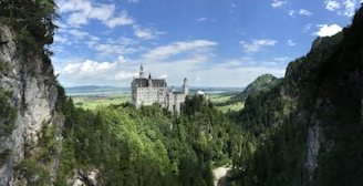 A majestic fantasy castle nestled among lush green forests under a bright blue sky