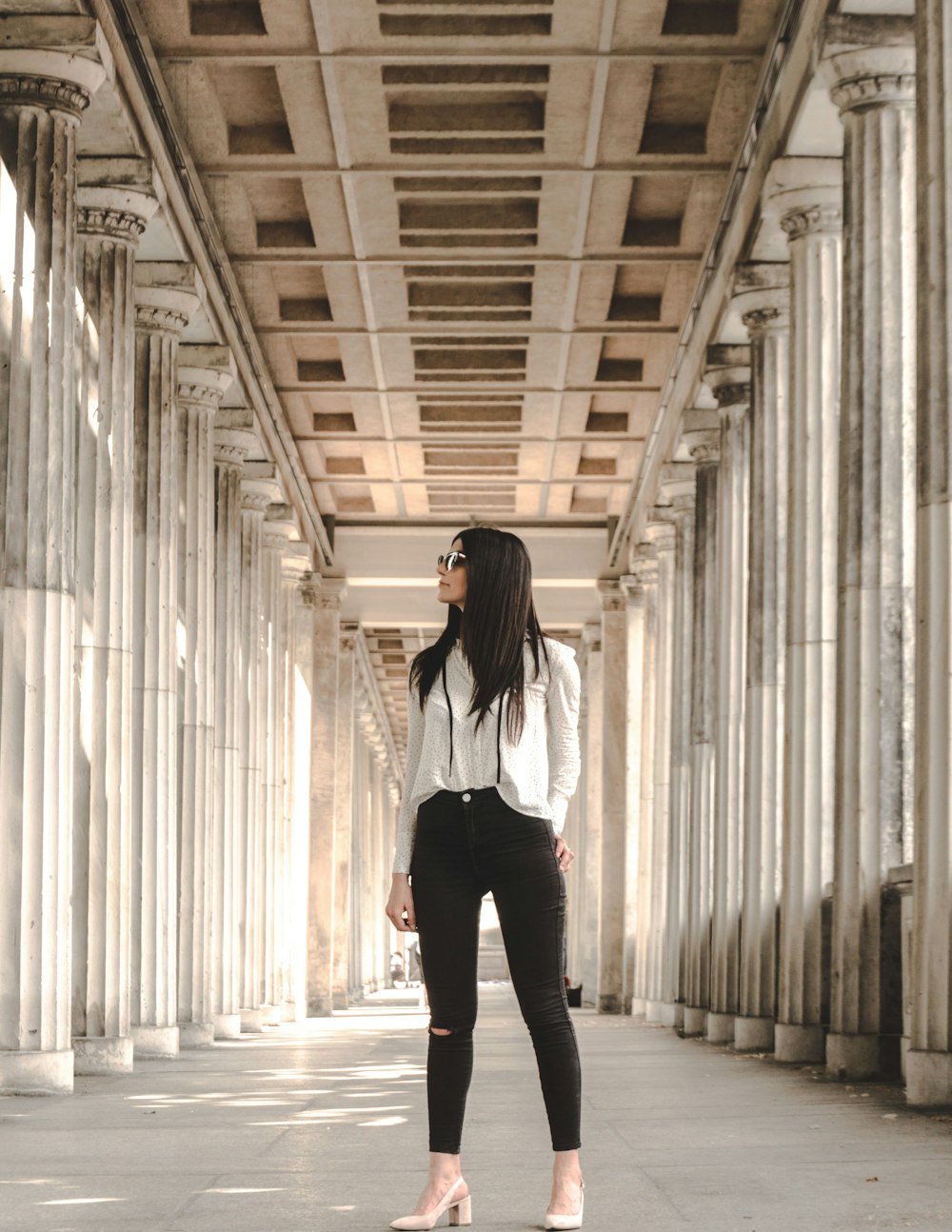 woman in white long-sleeved shirt and black pants standing in between pillars