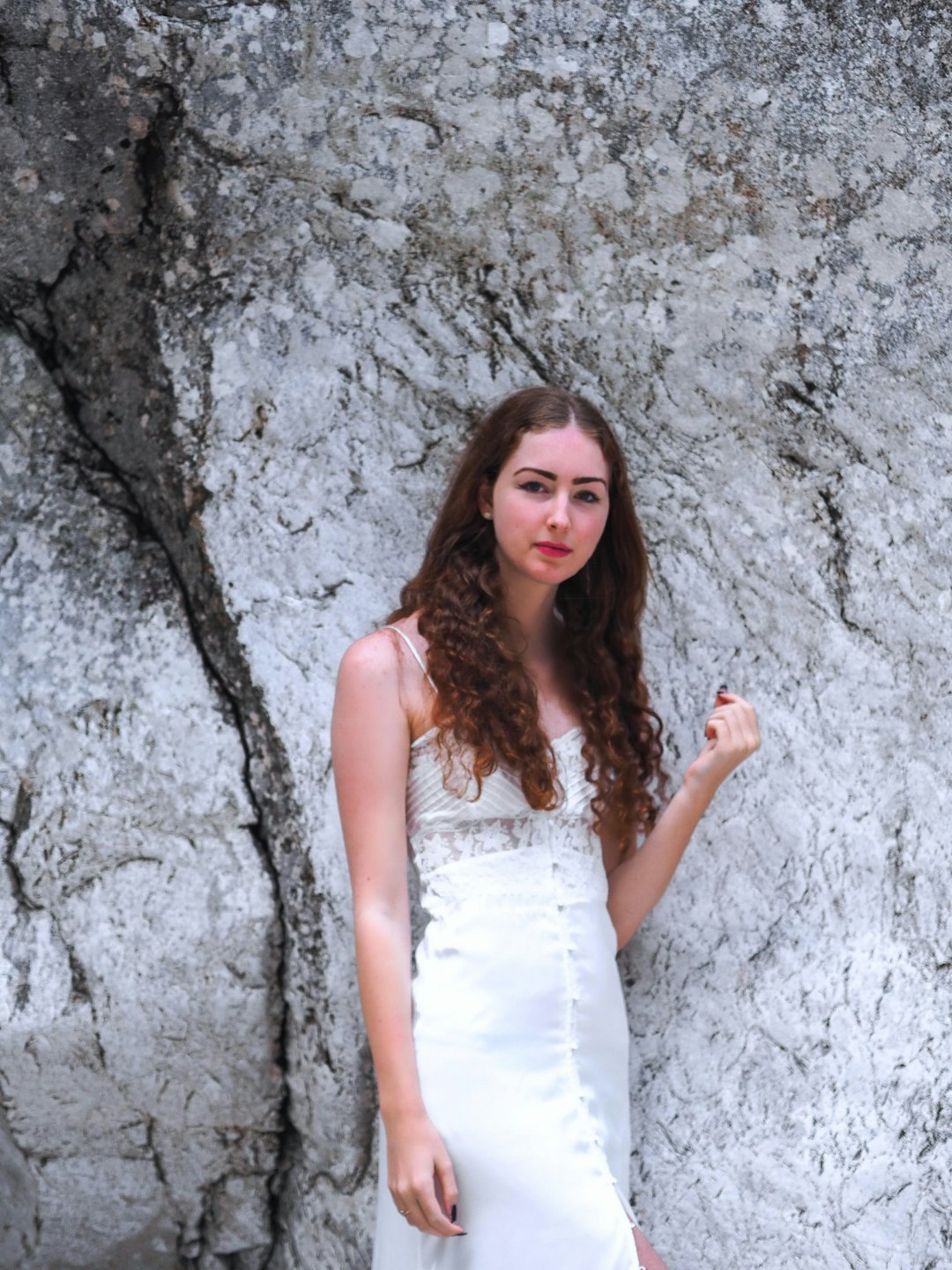 woman wearing white spaghetti strap dress standing near gray rock