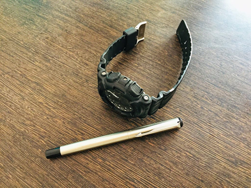 A close-up of a stylish men's watch resting on a wooden table beside a notebook and pen.