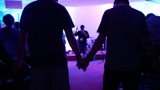 A small circle of people holding hands in a warm, softly lit room.