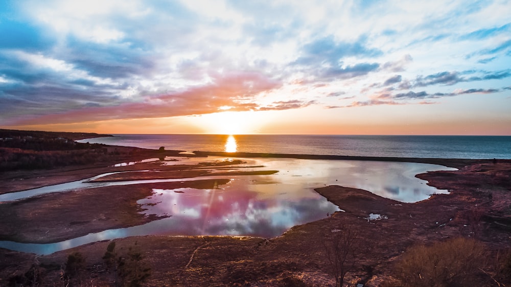 calm water with brown shoreline under cloudy sky