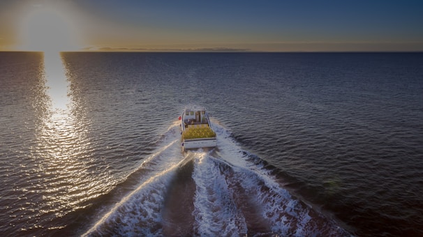 A ship navigating through open waters with the sun setting on the horizon.