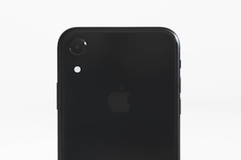A close-up of the back of a black smartphone, displaying the rear camera and flash. The phone's surface reflects light, with the logo subtly visible in the center.
