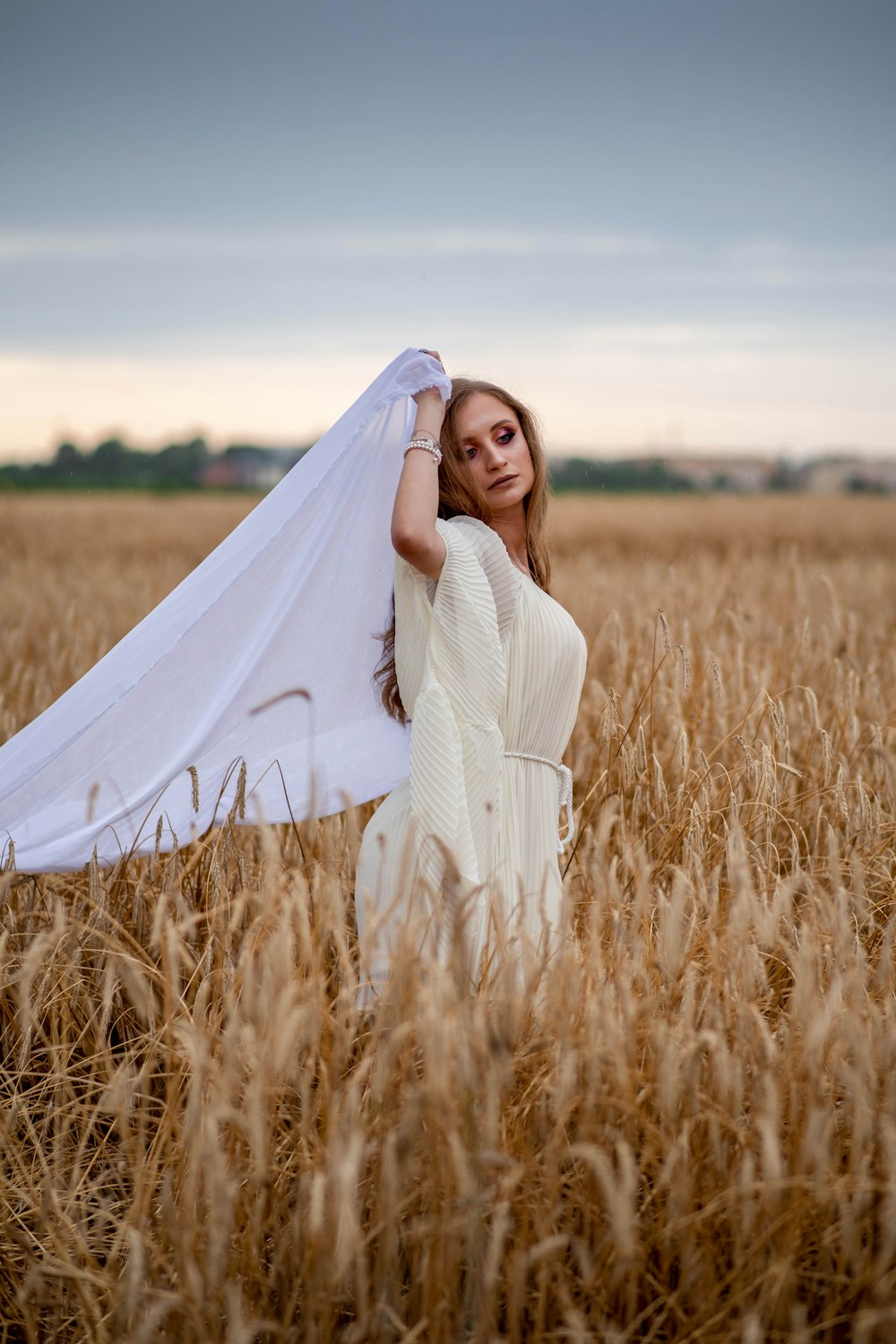 woman standing on wheat field while raising white textile at her back