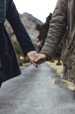 two person holding hands while walking on asphalt road