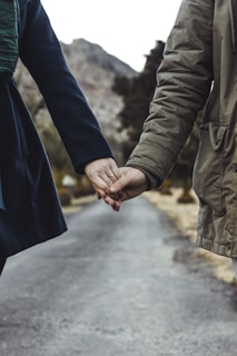 two person holding hands while walking on asphalt road