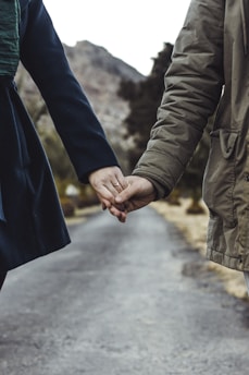 two person holding hands while walking on asphalt road