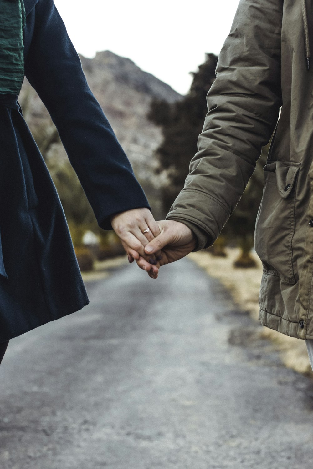 due persone che si tengono per mano mentre camminano sulla strada asfaltata