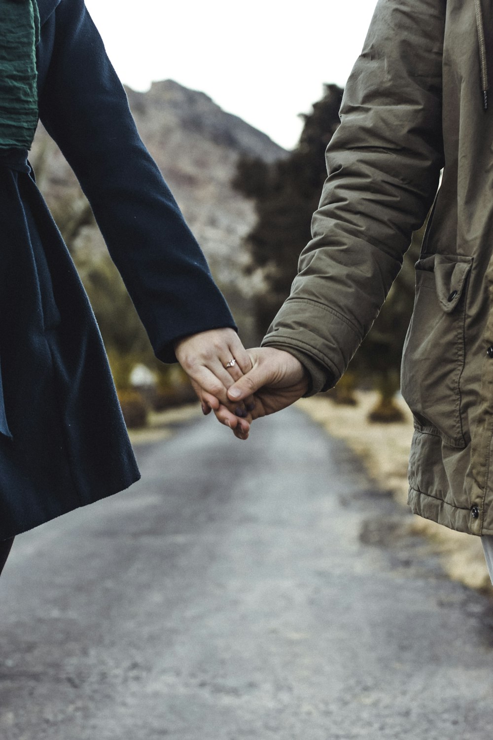 two person holding hands while walking on asphalt road