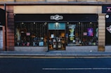 A storefront with black signage displays the logo for a shop named 'Beyond' with the number 88. The large glass windows reveal a glimpse inside, where various items and posters are visible. Strings of lights hang down, adding a festive touch. The sidewalk and street are in the foreground.
