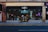 A storefront with black signage displays the logo for a shop named 'Beyond' with the number 88. The large glass windows reveal a glimpse inside, where various items and posters are visible. Strings of lights hang down, adding a festive touch. The sidewalk and street are in the foreground.