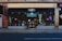 A storefront with black signage displays the logo for a shop named 'Beyond' with the number 88. The large glass windows reveal a glimpse inside, where various items and posters are visible. Strings of lights hang down, adding a festive touch. The sidewalk and street are in the foreground.