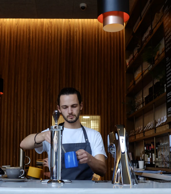 Barista mengenakan celemek AFUN di balik mesin espresso
