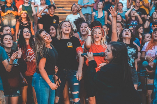A group of enthusiastic people gathered together, appearing joyful and engaged in a lively event. Many individuals are smiling, singing, and raising their hands in celebration. The atmosphere is festive and vibrant.