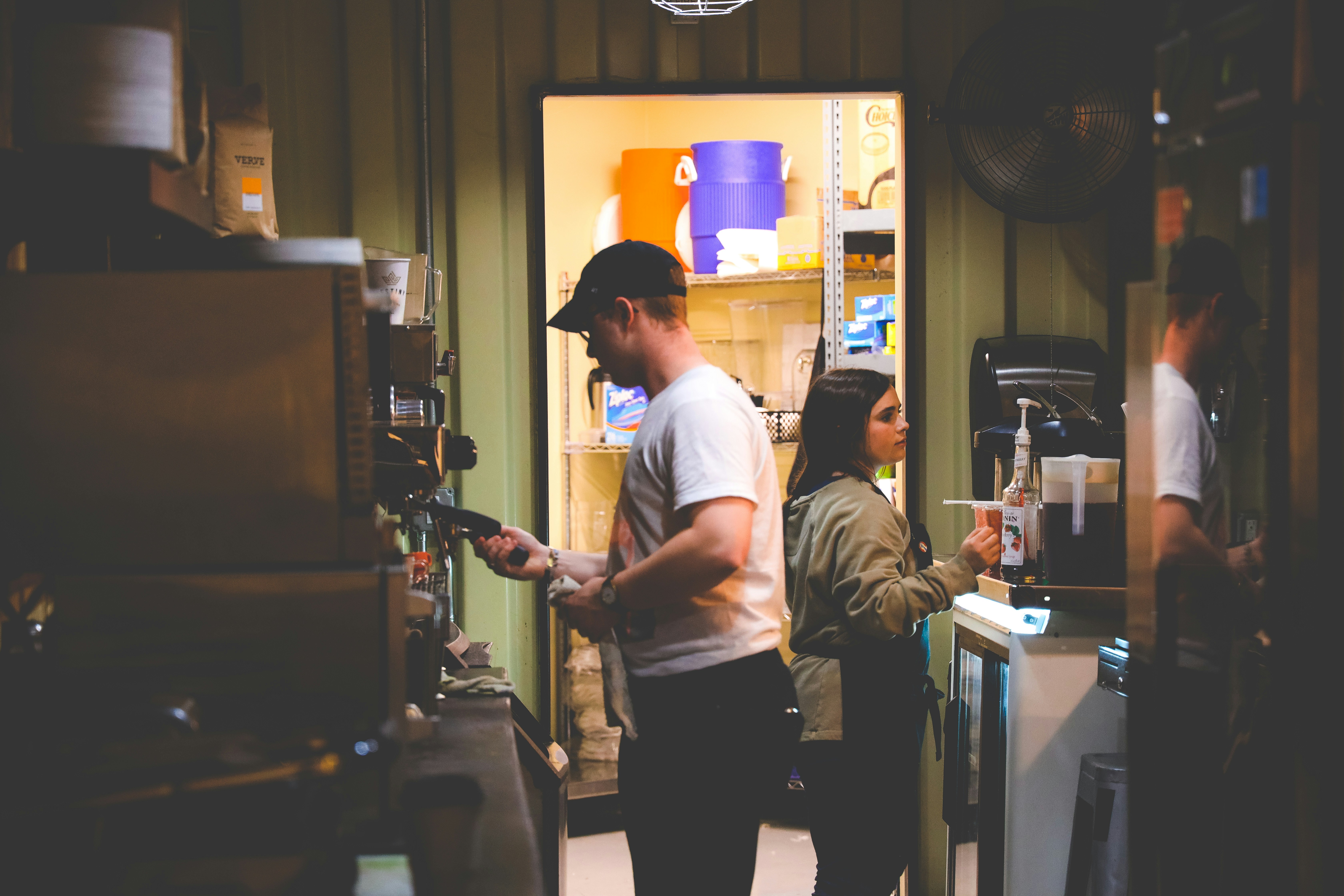 Back-of-house storage room of a small cafe with stocked shelves and two operators