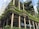 An urban architectural structure features multiple levels clad with lush green vegetation, interspersed with sleek, modern glass and metal elements. The building utilizes a blend of organic and contemporary design, highlighting vertical gardens and tiered plant arrangements.