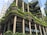 An urban architectural structure features multiple levels clad with lush green vegetation, interspersed with sleek, modern glass and metal elements. The building utilizes a blend of organic and contemporary design, highlighting vertical gardens and tiered plant arrangements.