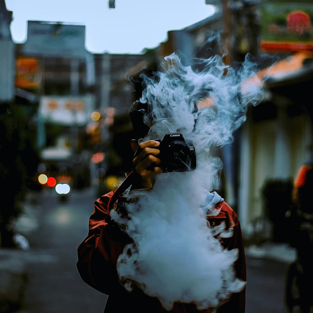 man breathing smoke and holding Canon camera covering his face