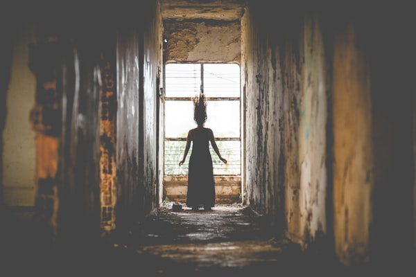 a figure with a wood-branch-like headdress against a window at the end of a grimy, abandoned hallway