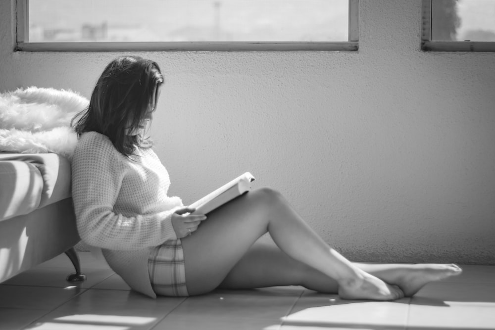 woman reading book sitting on floor beside furniture