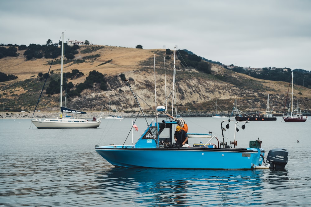 blue boat in body of water near boat and hill during daytime