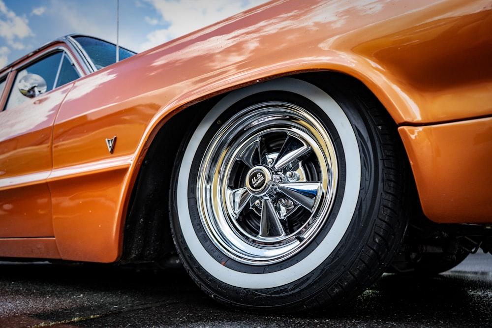 an orange car with chrome rims parked in a parking lot