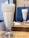 A close-up view of two tall, frothy milkshakes or smoothies served in clear glass cups. The glasses are placed on a wooden table with paper placemats labeled Zest Cafe & Restaurant. Napkins and cutlery are visible in the background.
