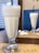 A close-up view of two tall, frothy milkshakes or smoothies served in clear glass cups. The glasses are placed on a wooden table with paper placemats labeled Zest Cafe & Restaurant. Napkins and cutlery are visible in the background.