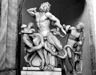 A classical marble sculpture depicting three human figures in dramatic poses, entangled with large serpents. The central figure appears to be in distress while the other two figures are similarly struggling, conveying a sense of movement and tension.