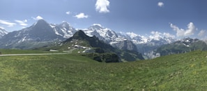 A panoramic view of snow-capped Himalayan peaks under a clear blue sky, with a winding trekking path below.