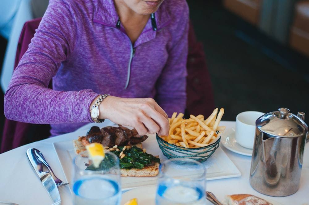 person eating cooked fries beside grilled meat