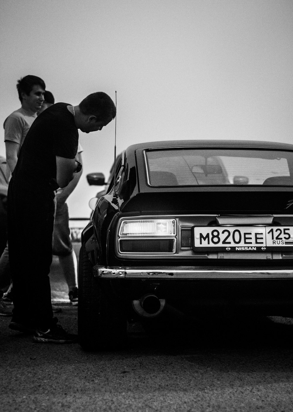 persone in piedi vicino alla foto in scala di grigi dell'auto d'epoca