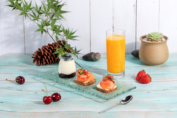 Orange juice in glass near pinecone, green succulent plant, cherry fruits, and gray stainless steel spoon