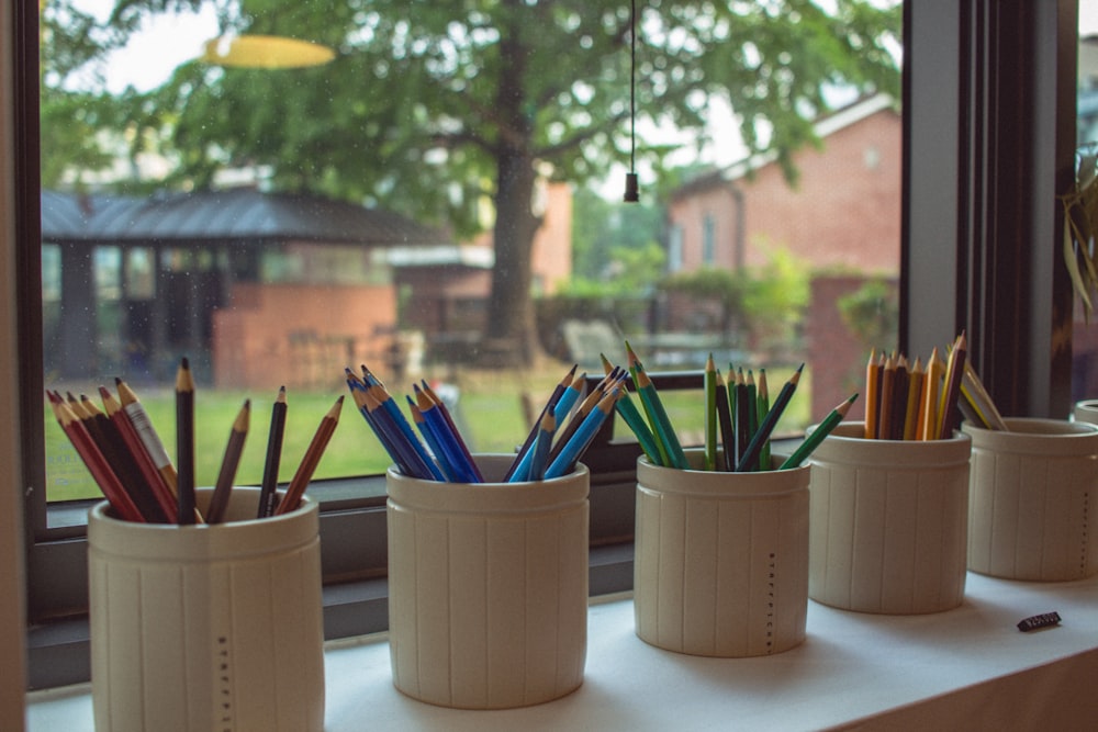 five cylindrical white ceramic pencil containers