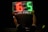 A person is holding up an electronic substitution board displaying the numbers 16 in red and 5 in green, typically used in football matches to indicate player changes.