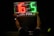 A person is holding up an electronic substitution board displaying the numbers 16 in red and 5 in green, typically used in football matches to indicate player changes.