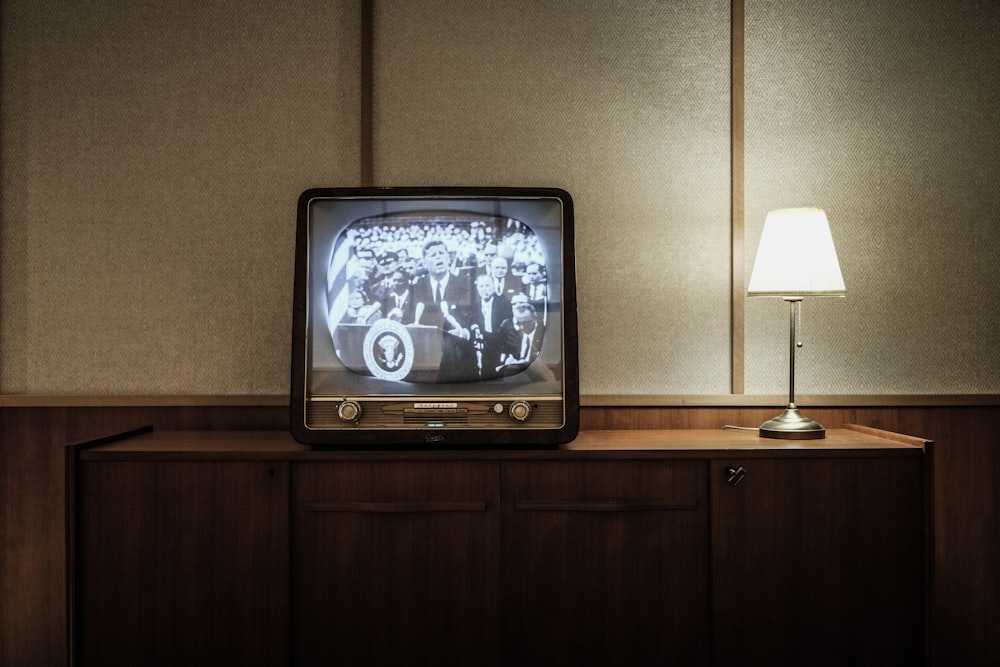 vintage black CRT TV turned-on near lighted table lamp