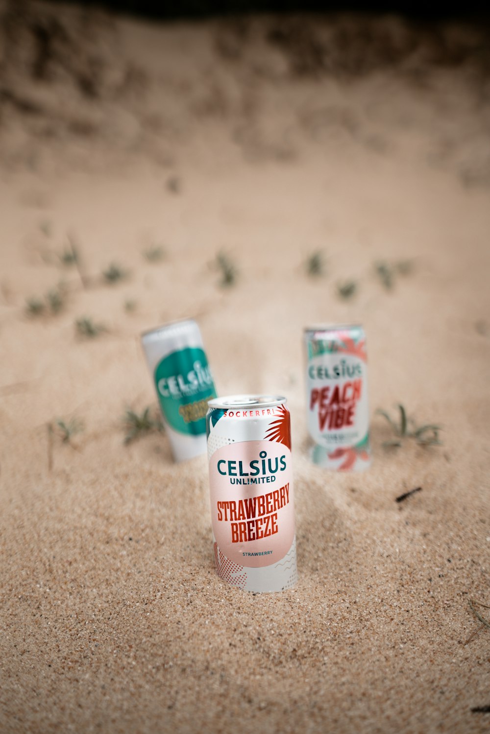 three cans of celsius sit in the sand