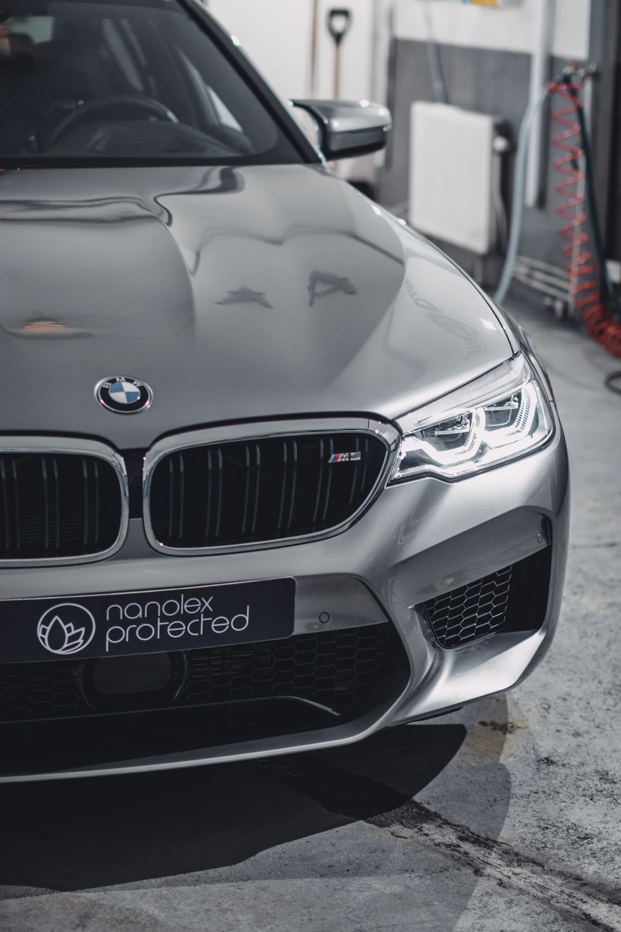 Sleek black car in a high-tech studio receiving a precise paint protection film application under blue electric lighting.