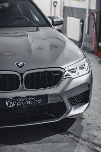Sleek black car in a high-tech studio receiving a precise paint protection film application under blue electric lighting.