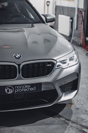 A sleek silver car with modern design featuring sharp headlights and a distinctive front grille. The branding 'nanolex protected' is visible on the front. The setting appears to be an indoor garage with tools and cables in the background.