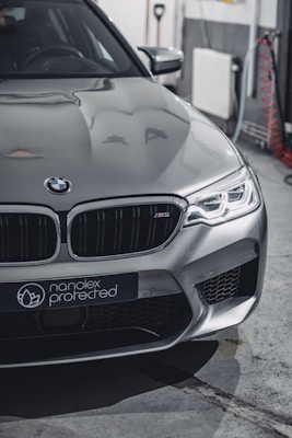 A sleek silver car with modern design featuring sharp headlights and a distinctive front grille. The branding 'nanolex protected' is visible on the front. The setting appears to be an indoor garage with tools and cables in the background.