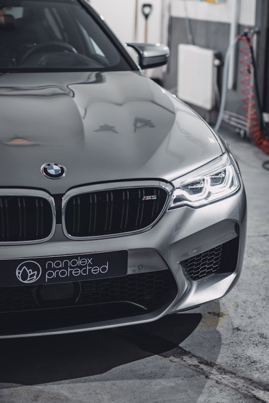 A sleek silver car with modern design featuring sharp headlights and a distinctive front grille. The branding 'nanolex protected' is visible on the front. The setting appears to be an indoor garage with tools and cables in the background.