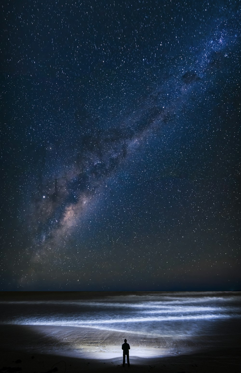 Un homme debout au sommet d’une plage sous un ciel nocturne