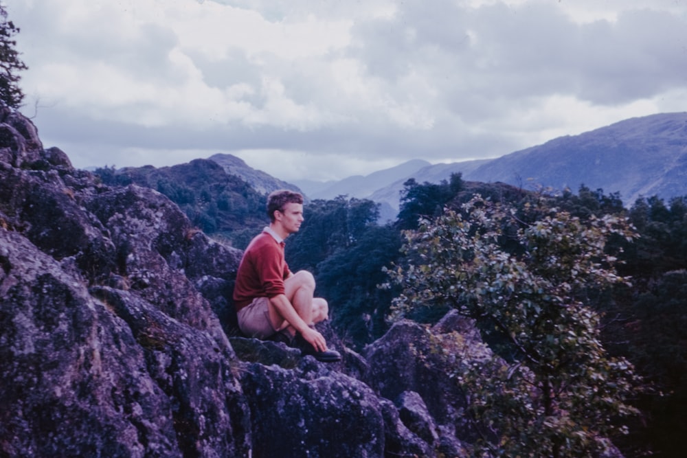man sitting on rocky hill looking straight on mountain